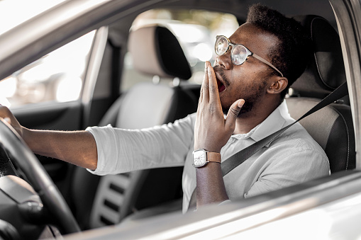 Sleepy fatigued yawning exhausted young man driving his car in traffic after a long hour drive. Transportation sleep deprivation accident concept
